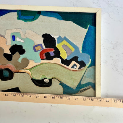 A framed abstract painting with geometric shapes in blue, green, beige, black, yellow, and red, shown on a white marble surface with a wooden ruler along the bottom edge for scale.