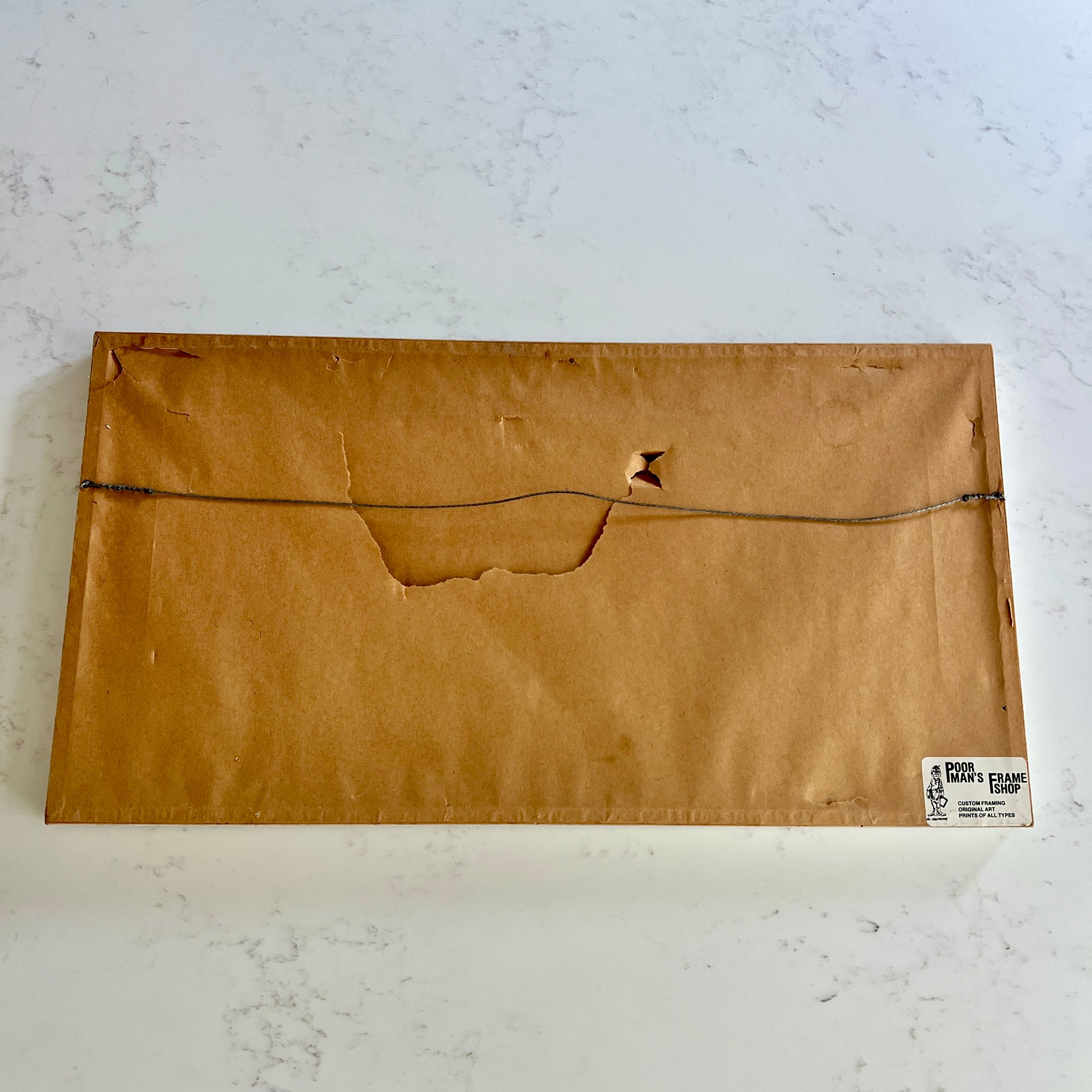 Back of frame with craft paper that is torn with wire hanger and sticker in the corner
