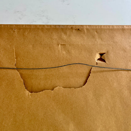 back of framed art showing torn brown paper and wire hanger