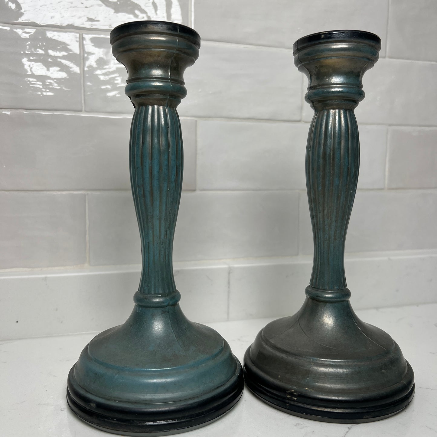 Two dark blue candle holders on a white surface with a tiled wall background