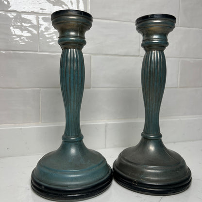 Two dark blue candle holders on a white surface with a tiled wall background
