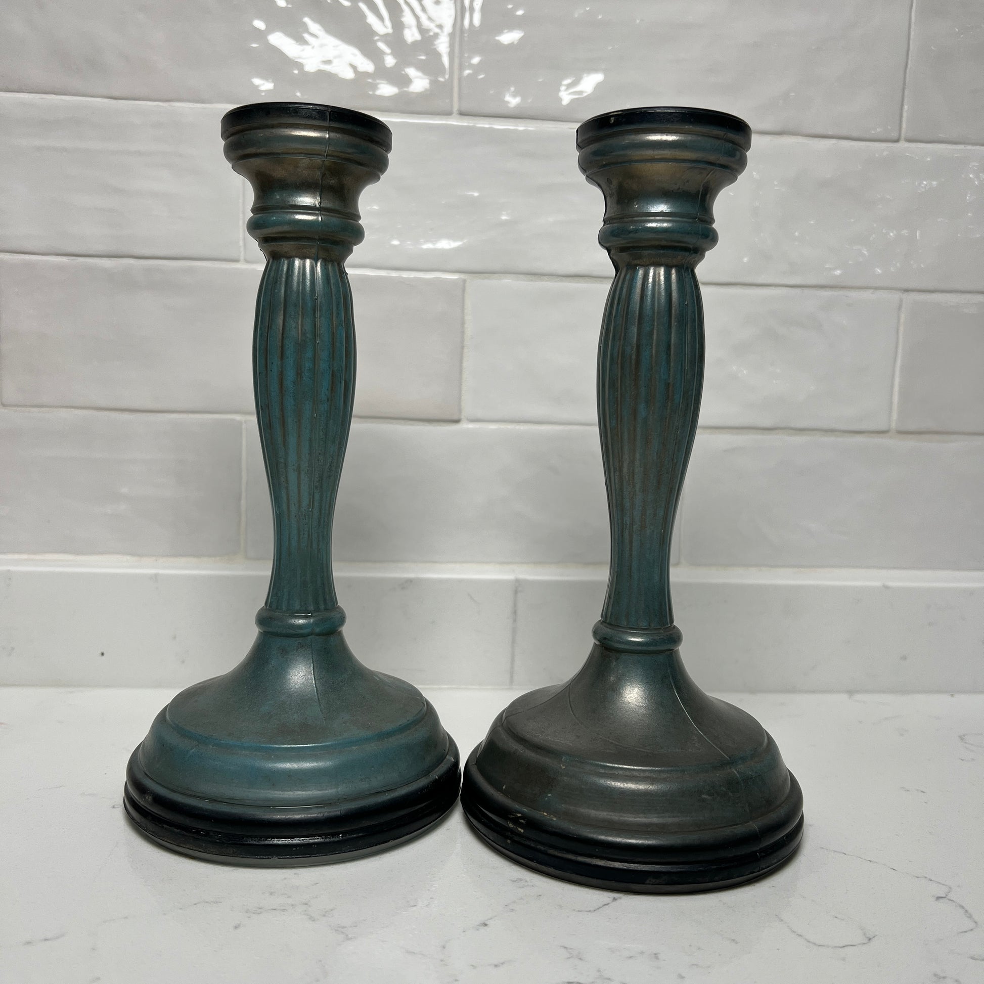 Two blue candle holders on a white surface with a tiled wall background