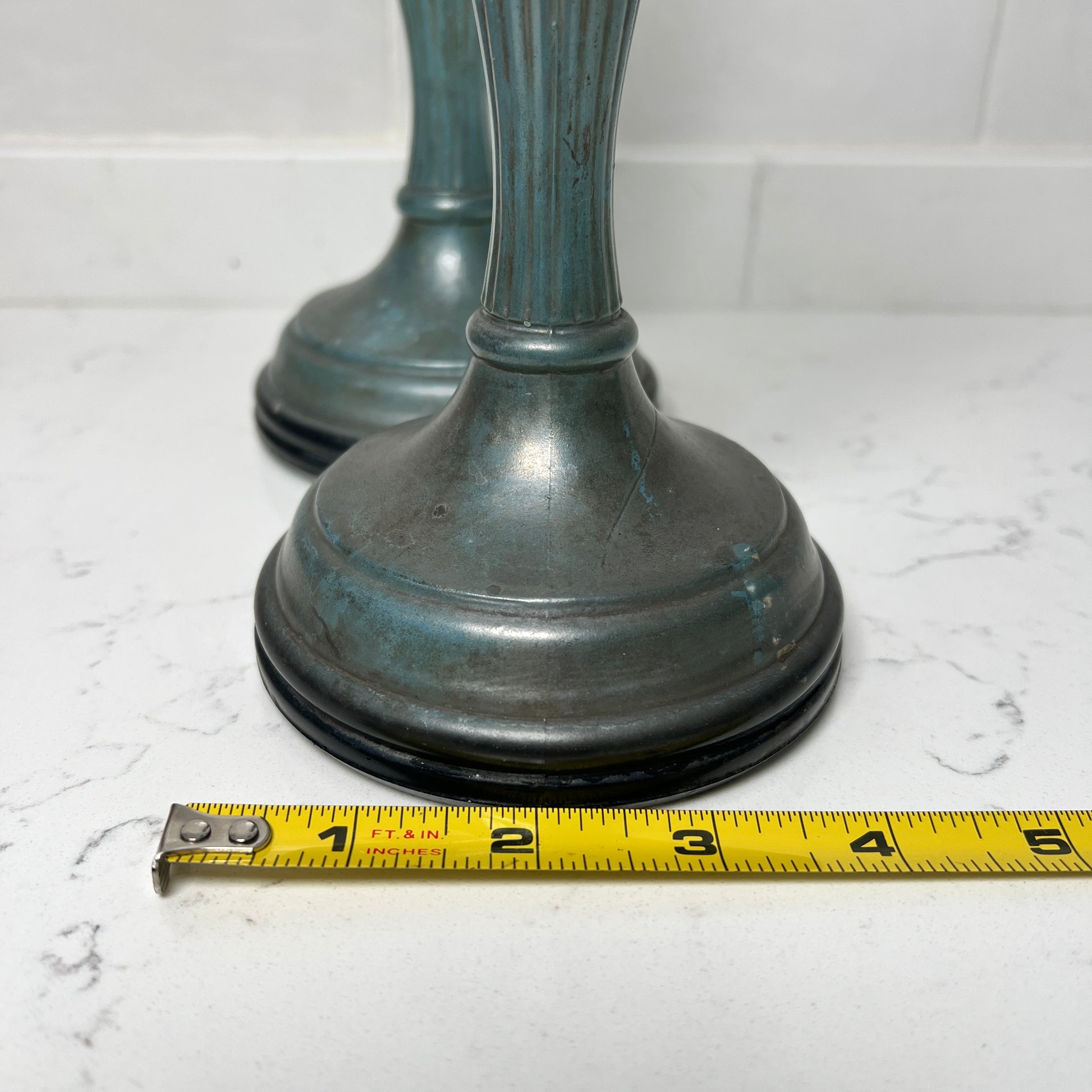 Two candle holders with a measuring tape for scale on a white marble surface.