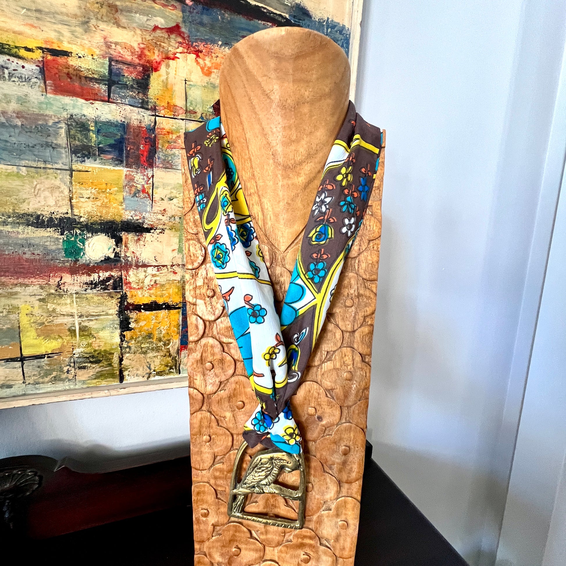 Mannequin head with a colorful scarf draped over it against a wall with abstract art.