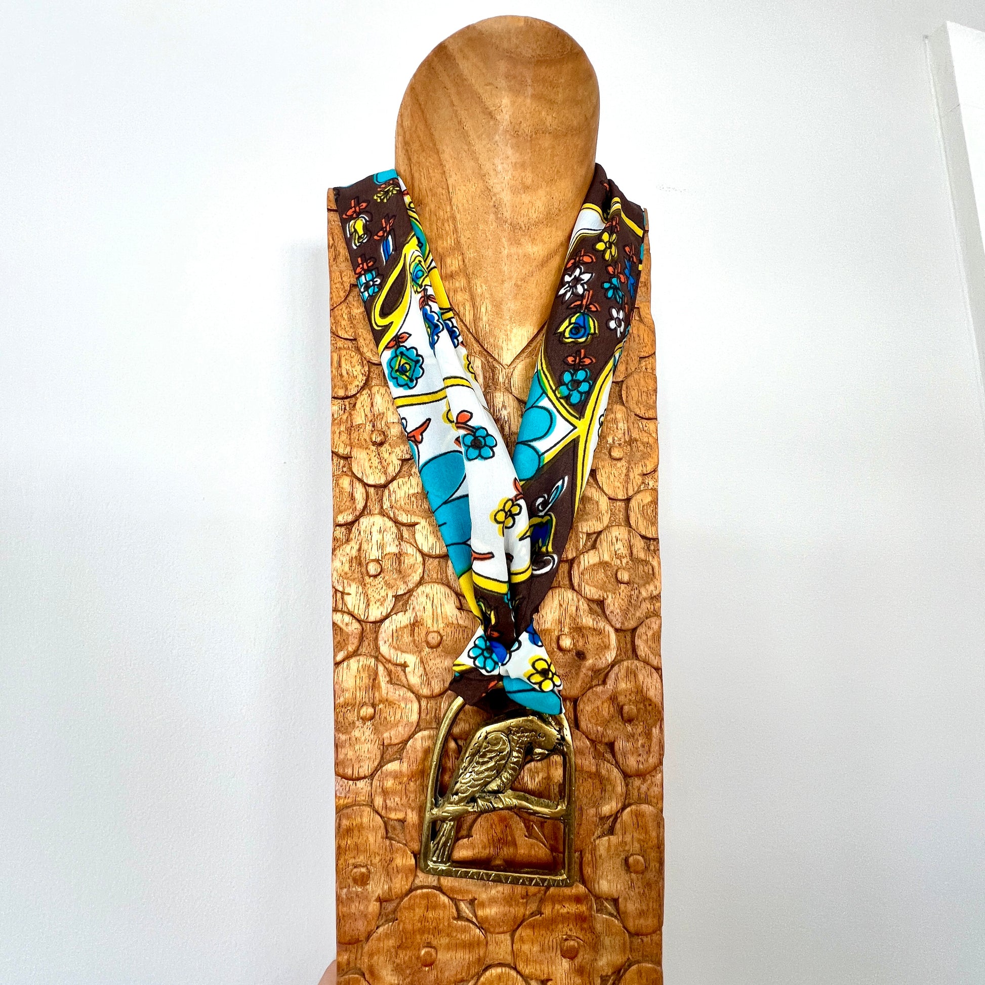 Colorful patterned scarf draped over a wooden mannequin head with a decorative base.