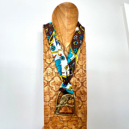 Colorful patterned scarf draped over a wooden mannequin head with a decorative base.