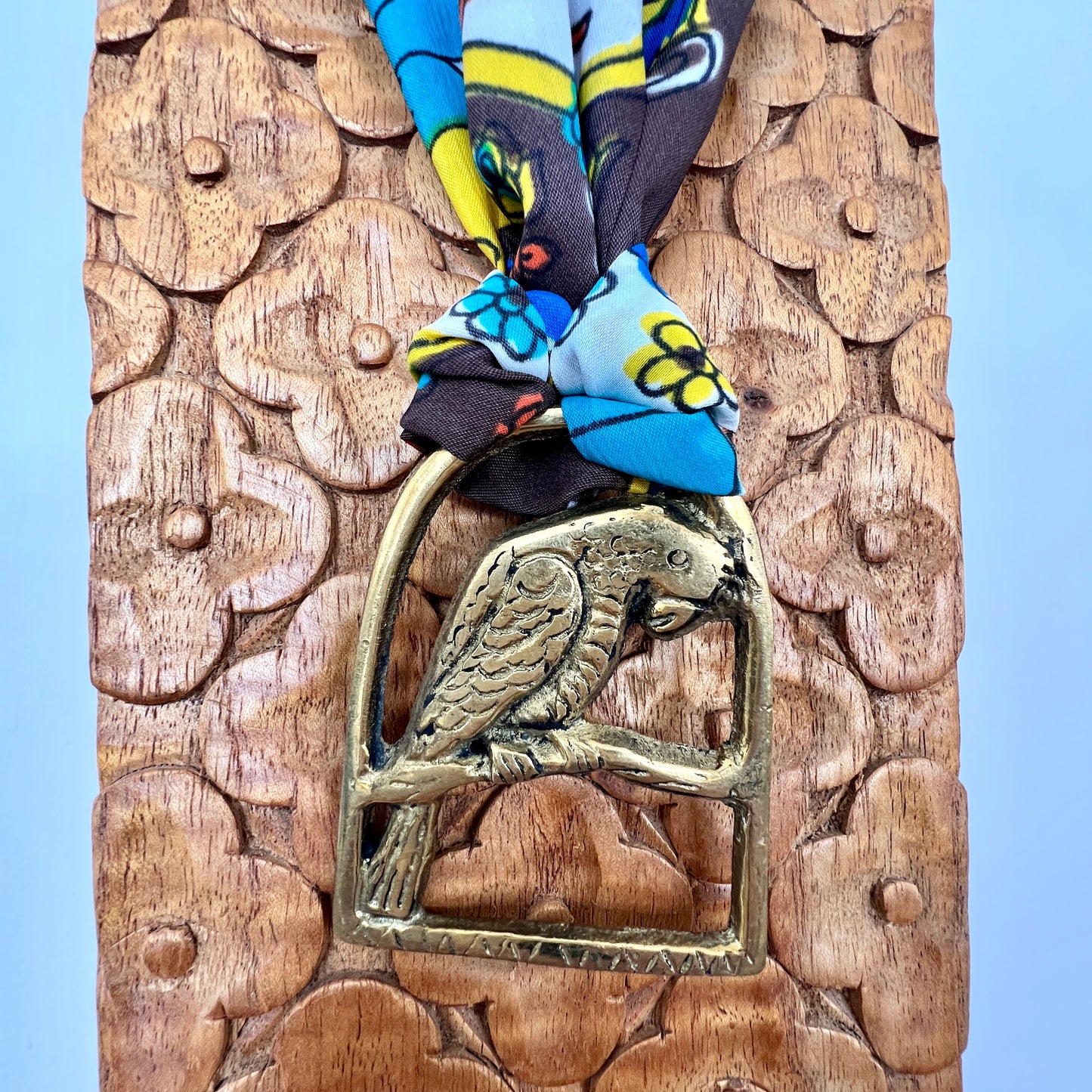 Decorative wooden panel with a brass parrot emblem and colorful fabric on top