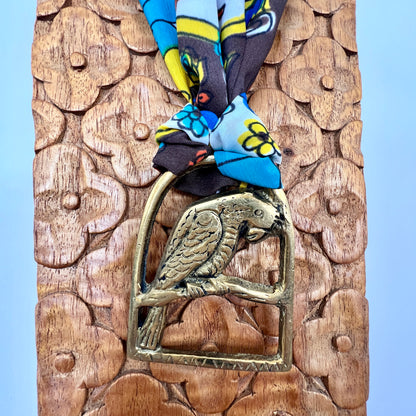 Decorative wooden panel with a brass parrot emblem and colorful fabric on top