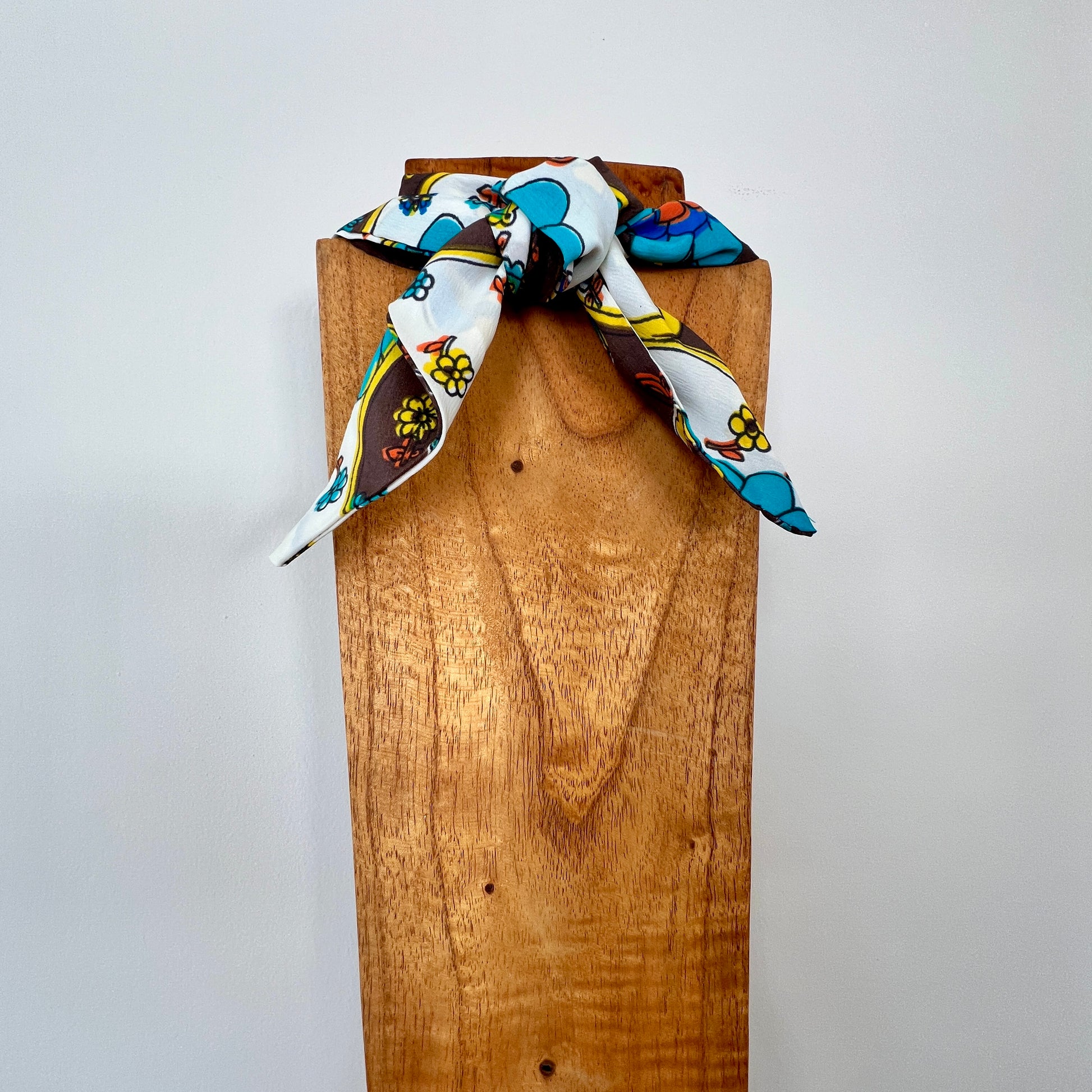 Colorful patterned scarf tied around a wooden block on a light gray background