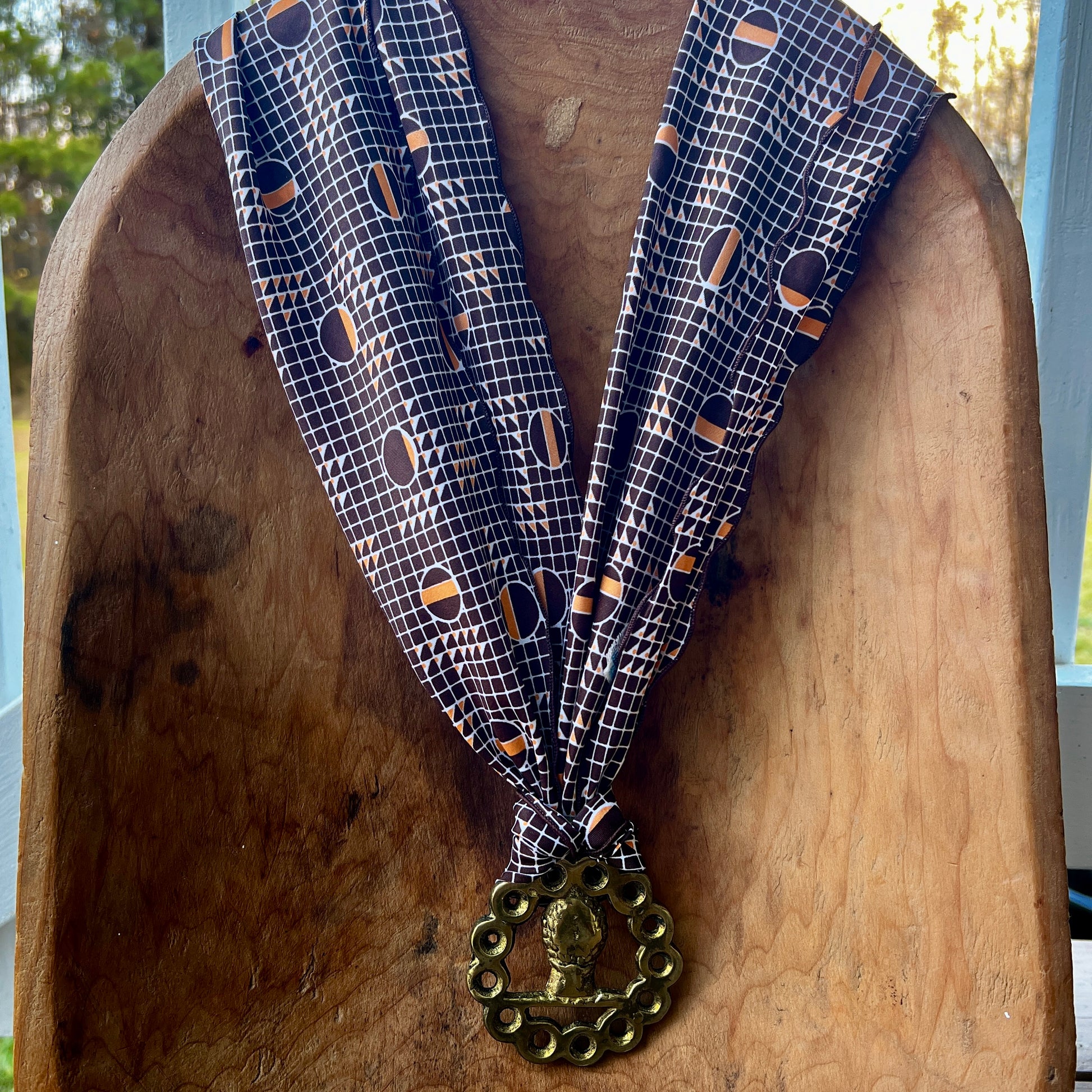 Vintage horse brass medallion necklace with geometric scarf, rustic equestrian jewelry on wooden surface
