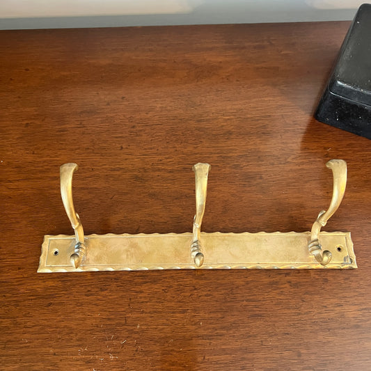 Brass coat rack with three hooks on a wooden surface