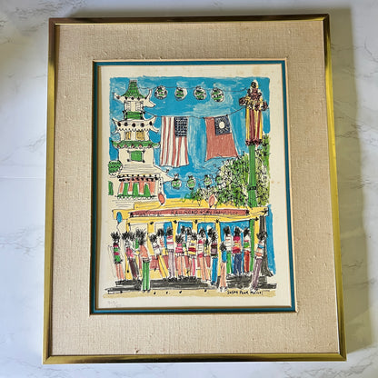 A framed folk art print depicting a street scene with a trolley, flags, and figures, mounted in a gold frame with a beige textured mat on a light marble surface.