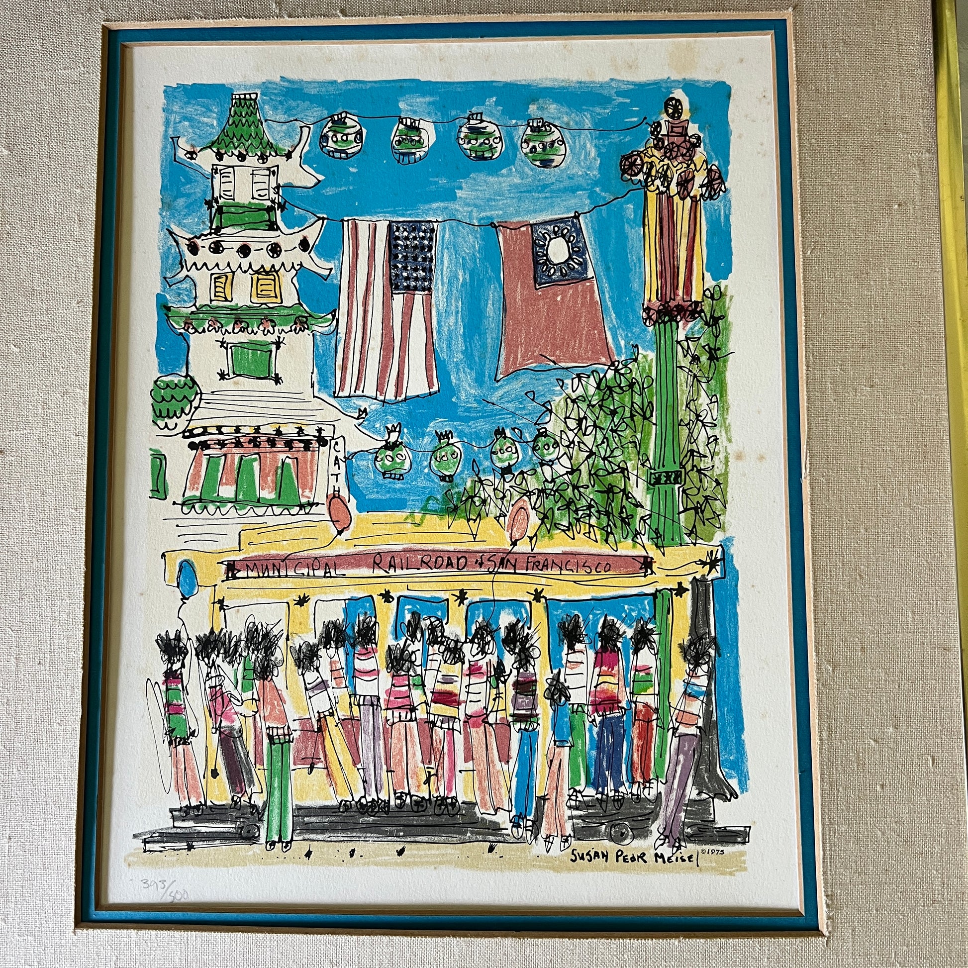 A framed folk art print depicting a street scene in San Francisco with a pagoda, hanging flags, a trolley, and figures walking along the street, mounted on a textured beige wall.