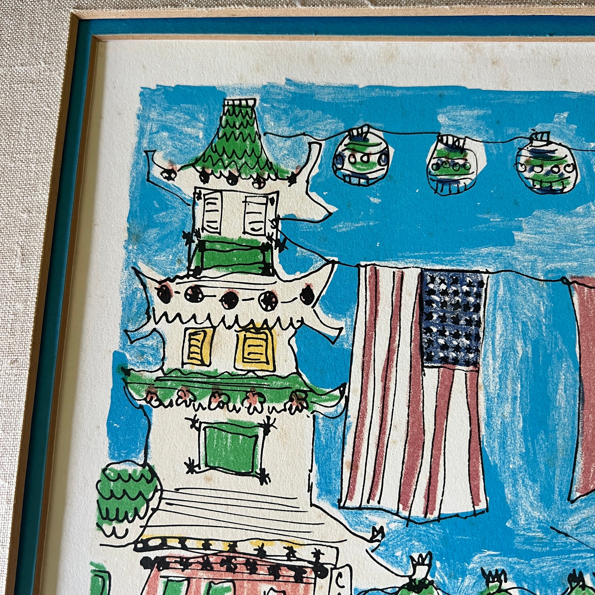 A framed children's hand-drawn style art print featuring a pagoda, an American flag, and hanging ornaments against a bright blue sky, shown in a close-up view with the frame edge visible.