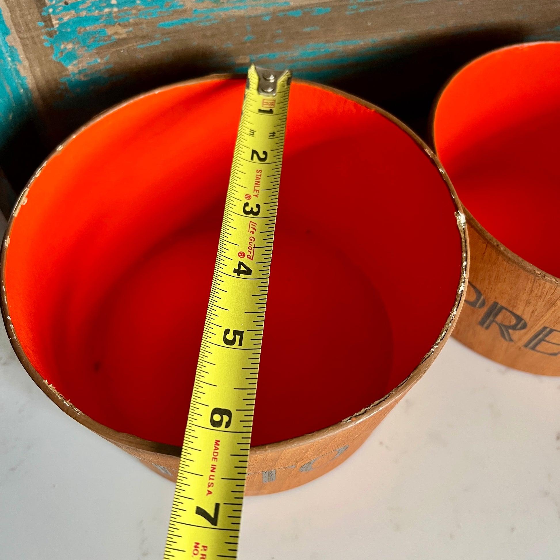 orange cylindrical container with a measuring tape indicating its diameter
