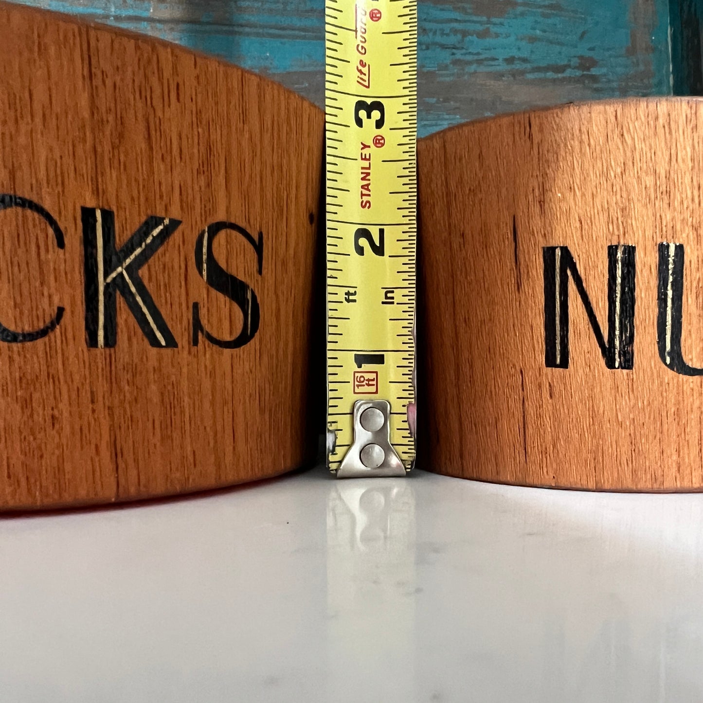 Two wooden bowls with letters and a measuring tape between them.