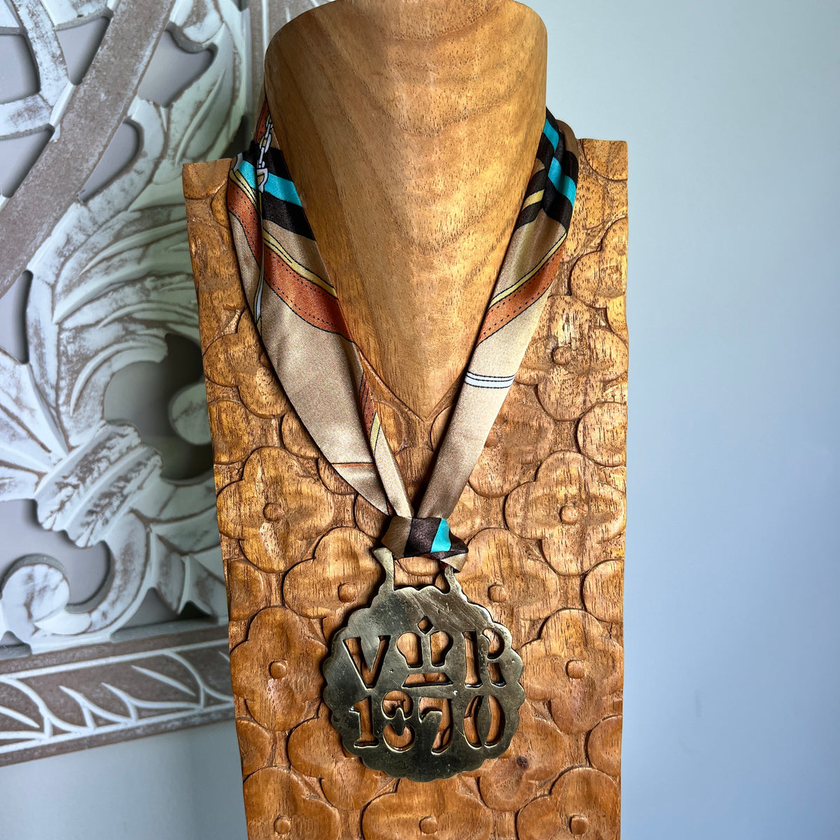A bronze-toned historical medal with a patterned silk ribbon displayed on a carved wooden stand. The medal features the engraved text 'V R 1870.
