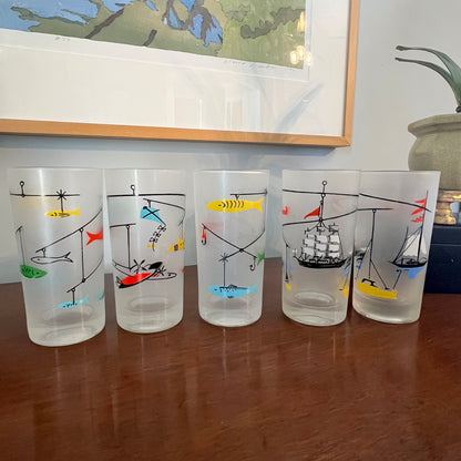 Set of five frosted glasses with colorful maritime designs on a wooden surface.