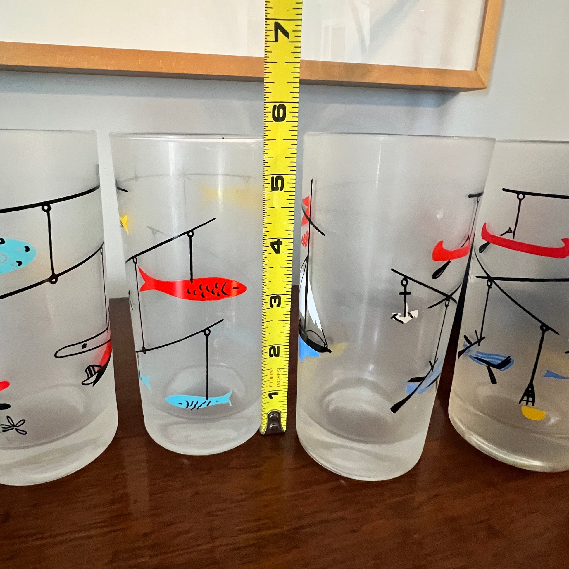 Four glass with fishing-themed designs and a measuring tape for scale.
