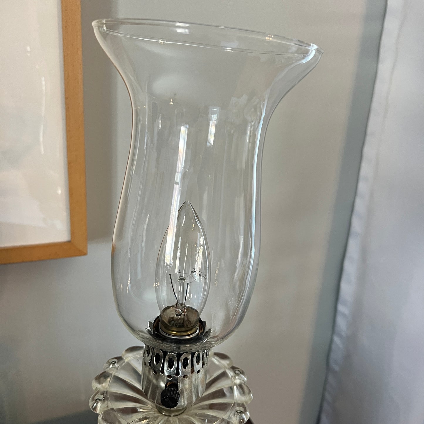 Clear glass hurricane lamp with a visible light bulb inside on a neutral background