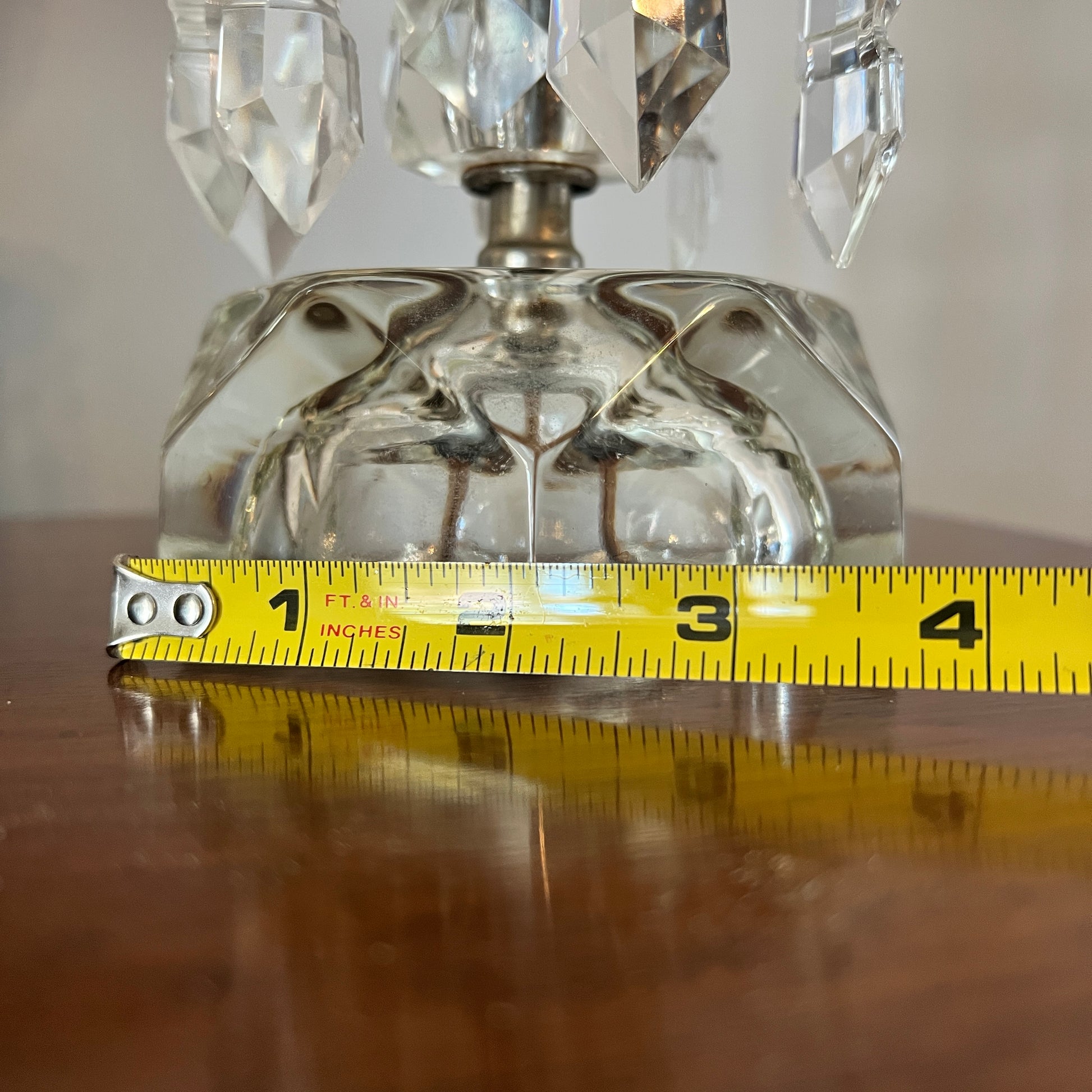 Clear glass lamp with crystal accents and a measuring tape for scale on a reflective surface.