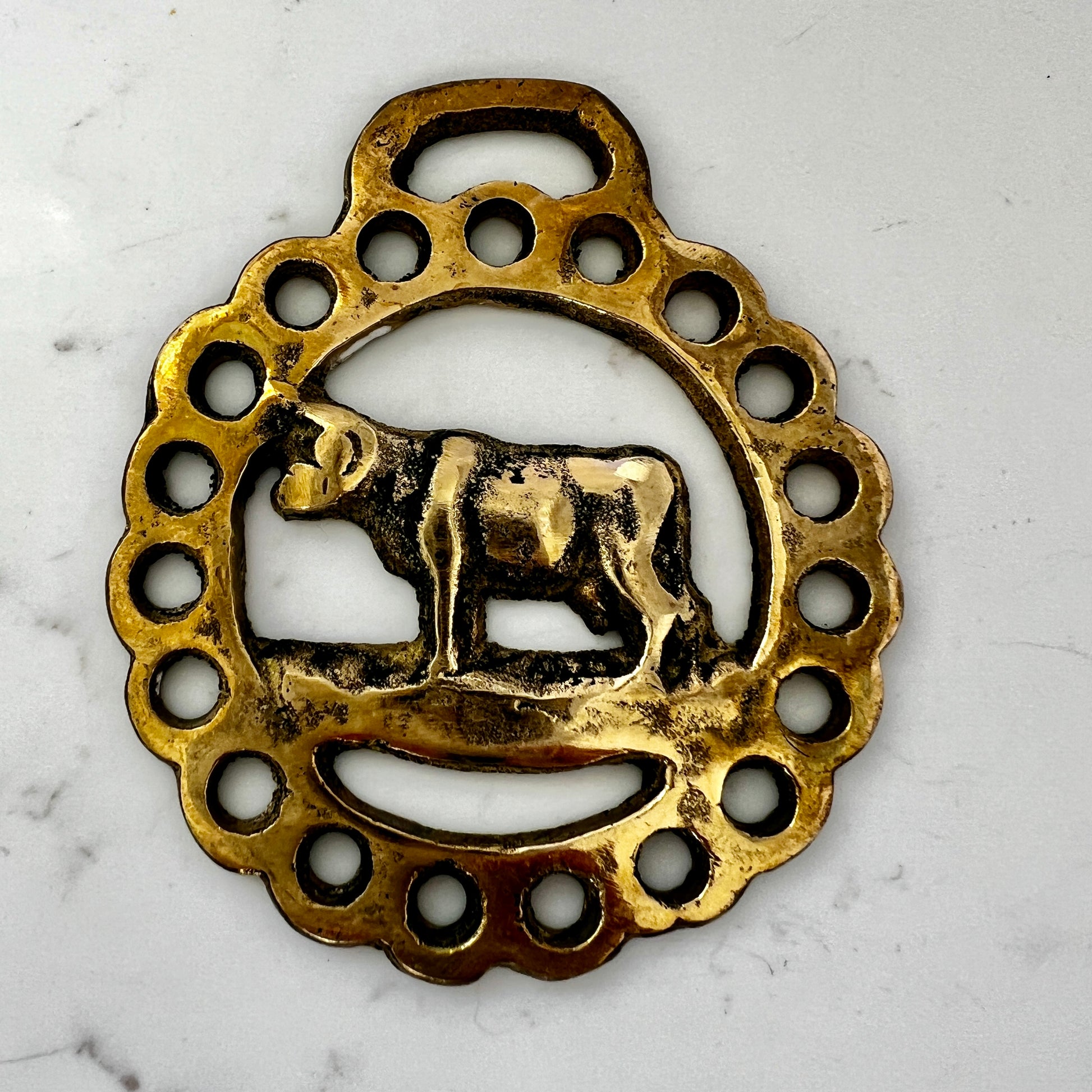 Decorative brass pendant with a cow design on a white marble background
