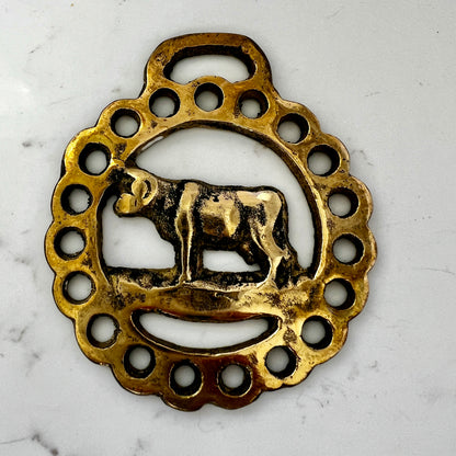 Decorative brass pendant with a cow design on a white marble background
