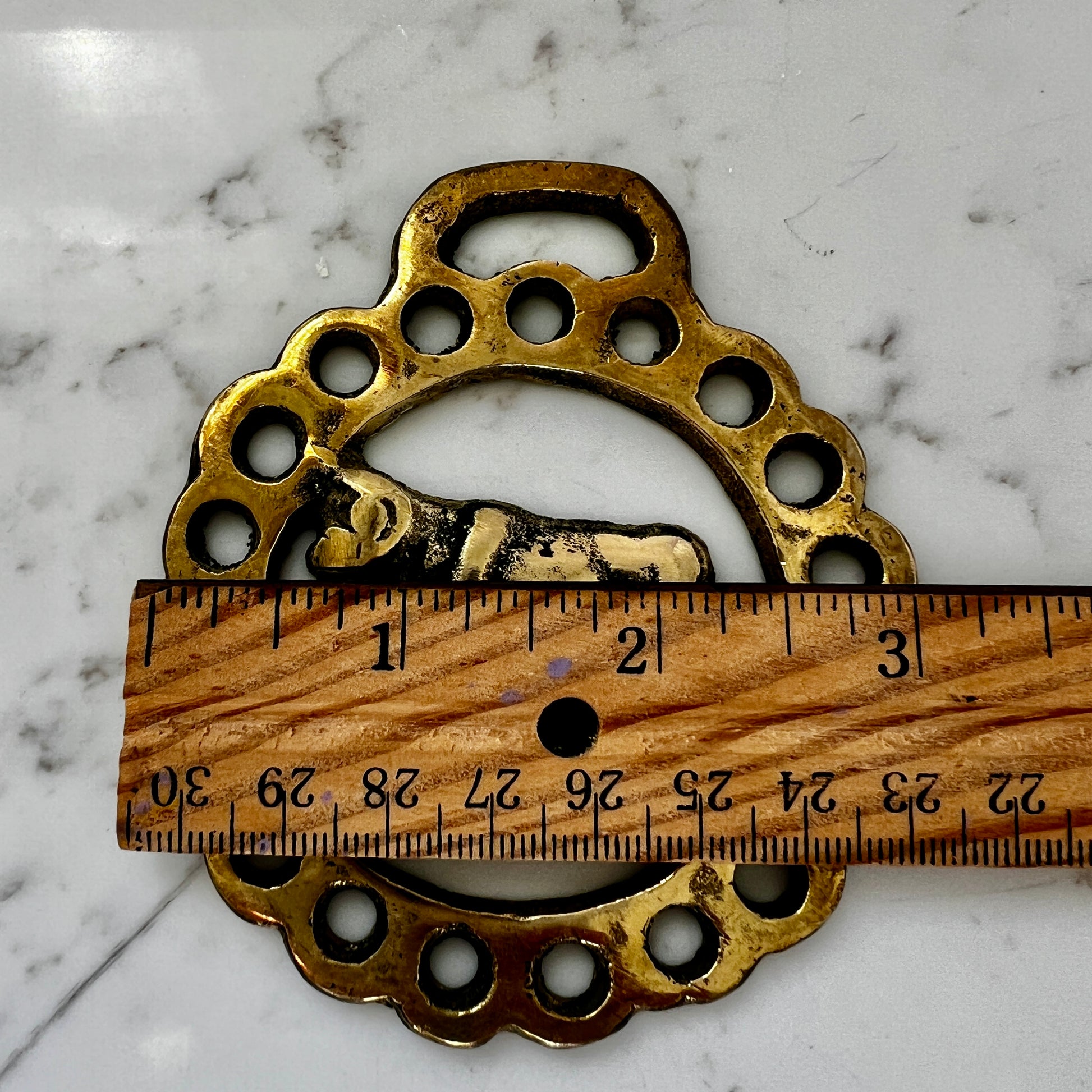 Brass medallion on a marble surface with a wooden ruler for scale.