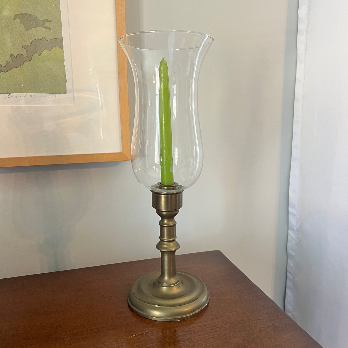 Decorative candle holder with a green candle on a wooden surface, with a framed picture in the background.