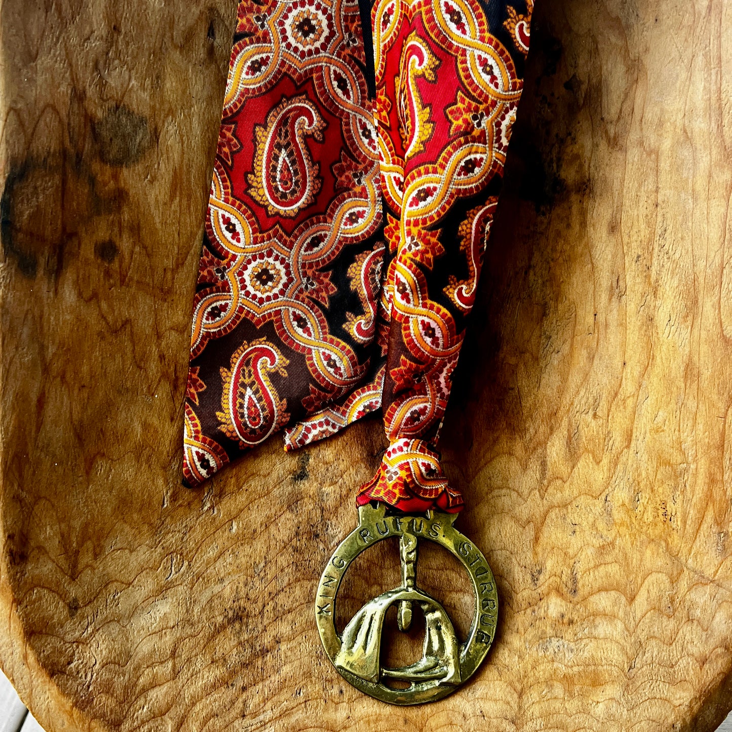 Red paisley tie with a decorative medallion on a wooden surface