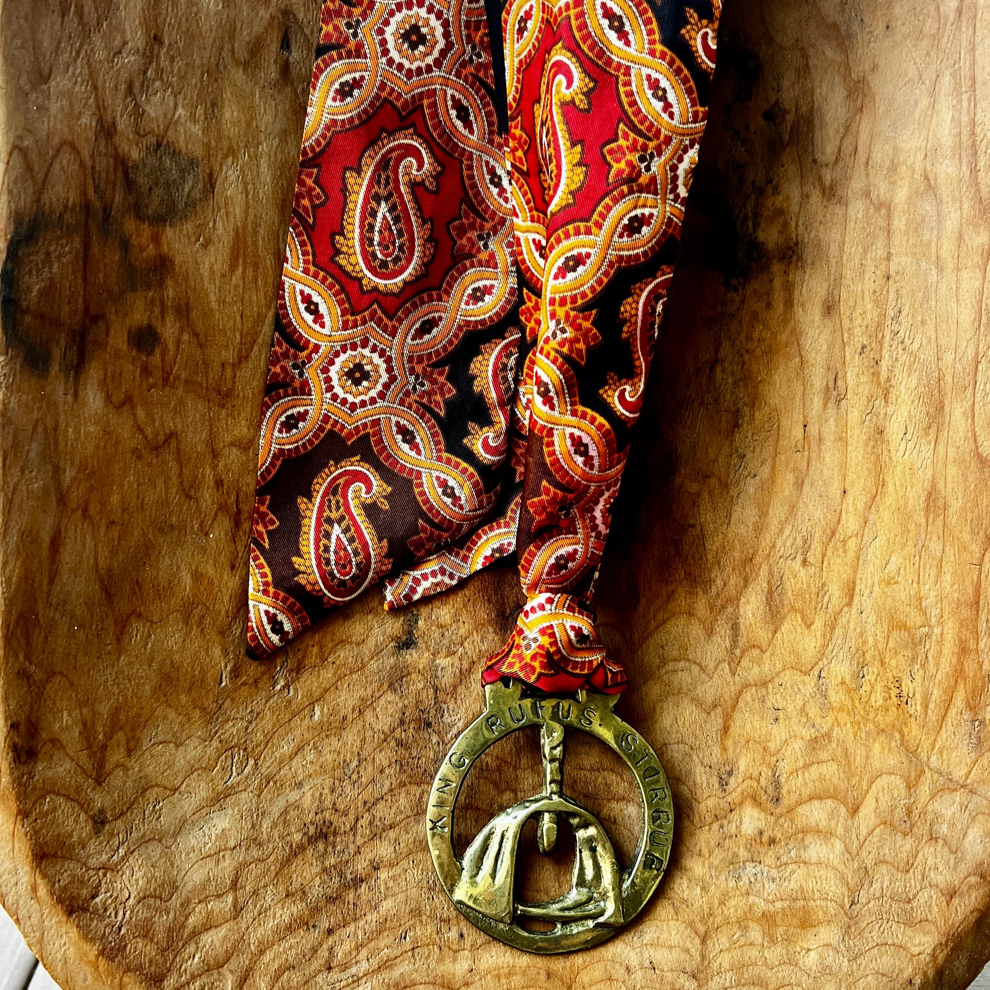 Red paisley tie with a decorative medallion on a wooden surface