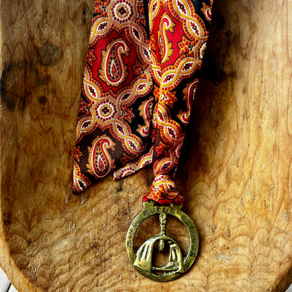 Red paisley tie with a decorative medallion on a wooden surface