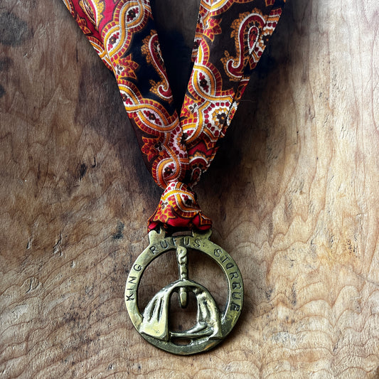 Medal with a stirrup design and 'King Ruffus Stirrup' text on a patterned ribbon against a wooden background