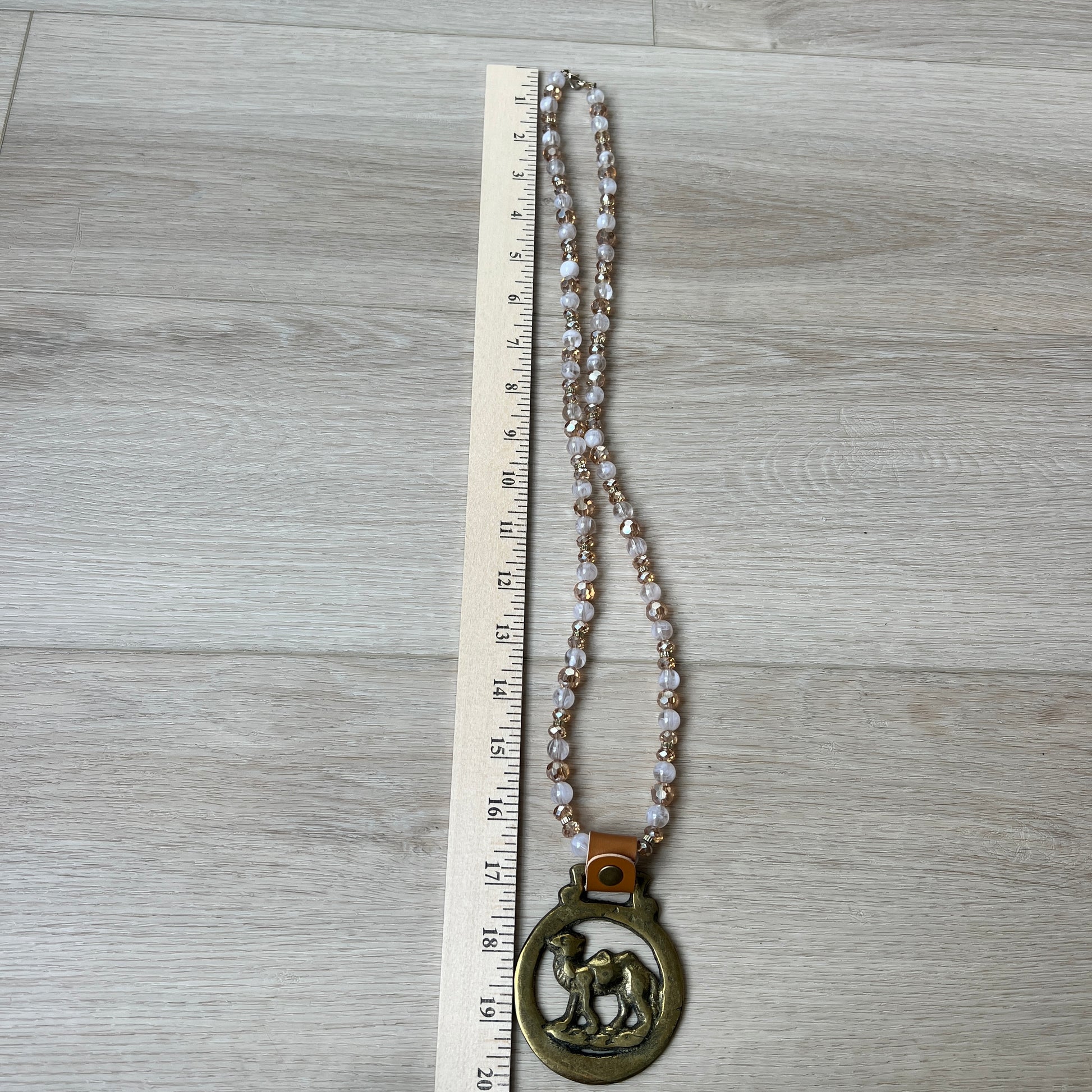 Necklace with a large pendant on a wooden surface next to a ruler for scale.