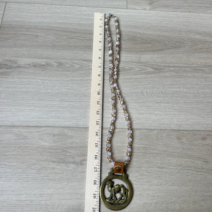 Necklace with a large pendant on a wooden surface next to a ruler for scale.