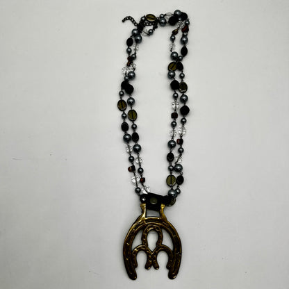 Vintage double horseshoe brass medallion necklace with dark multi-strand beads and leather connector.