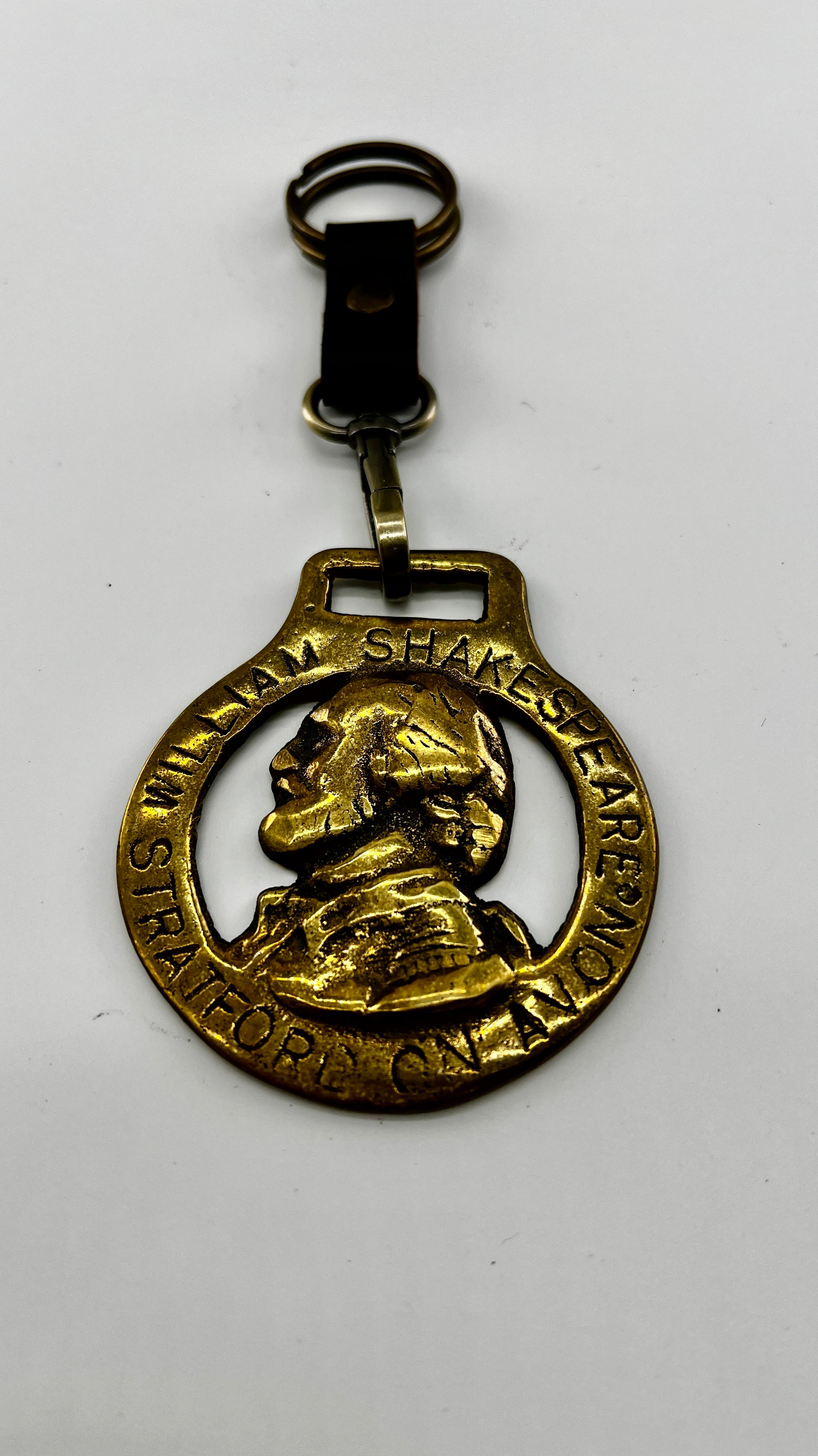 Vintage William Shakespeare horse brass medallion attached to brown leather keychain with brass ring and clip.