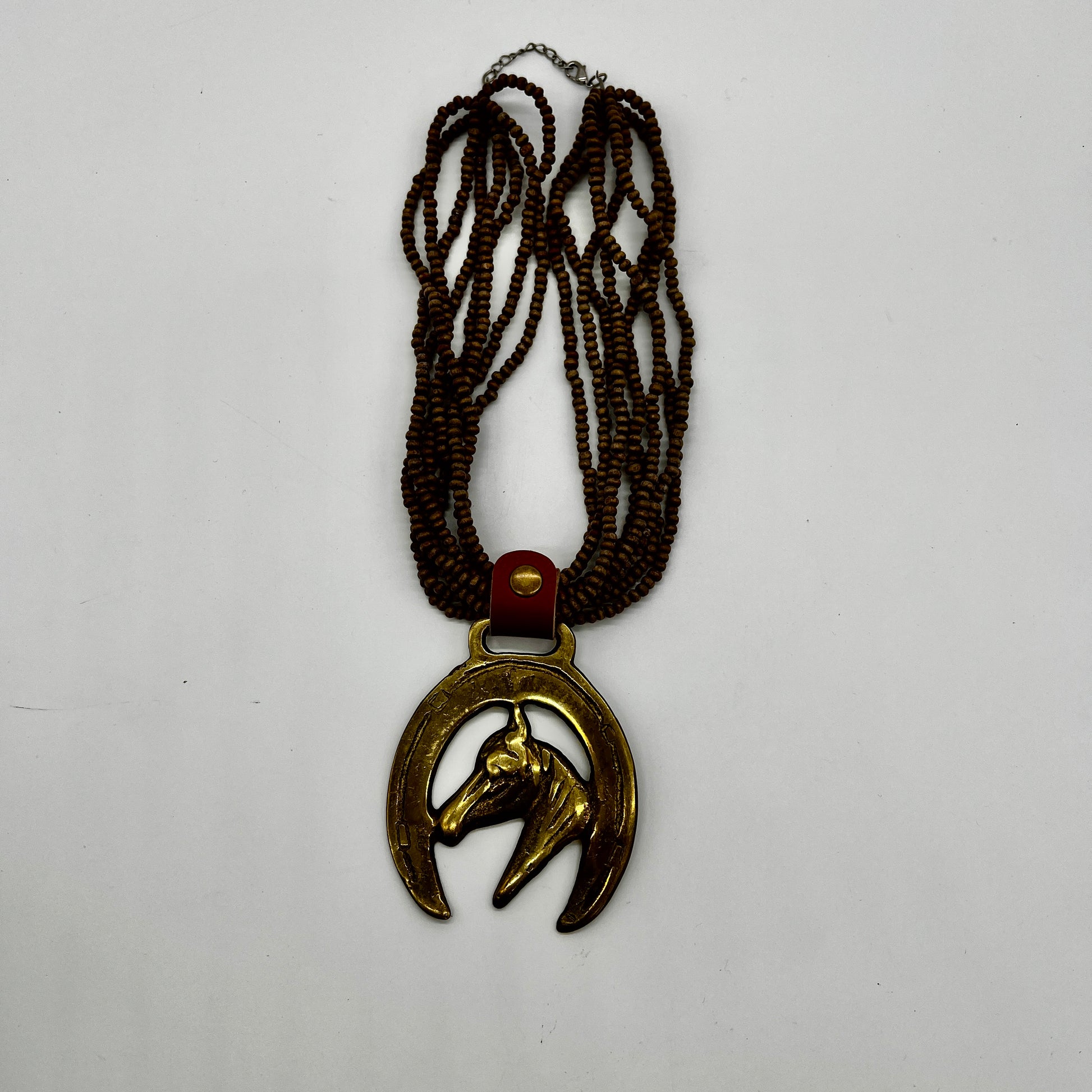 Vintage horse brass medallion attached to multi-strand wooden bead necklace with caramel leather connector.