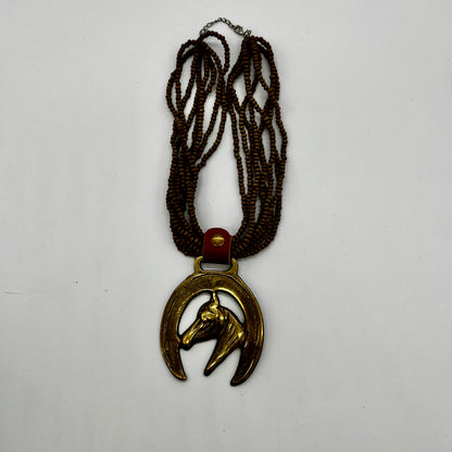 Vintage horse brass medallion attached to multi-strand wooden bead necklace with caramel leather connector.
