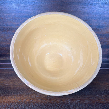 A handmade pottery bowl with a smooth, matte light beige interior and a textured, slightly rougher beige exterior, photographed from directly above on a dark wood background.