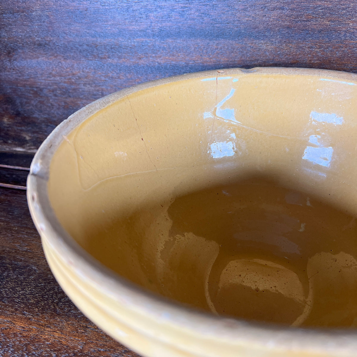 Close-up of the inside of a handmade bowl with a glossy, warm beige glaze, resting on a dark wooden surface.