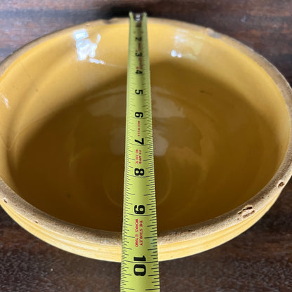 A yellow ceramic bowl with a measuring tape inserted vertically to show its depth, set against a dark wooden background.