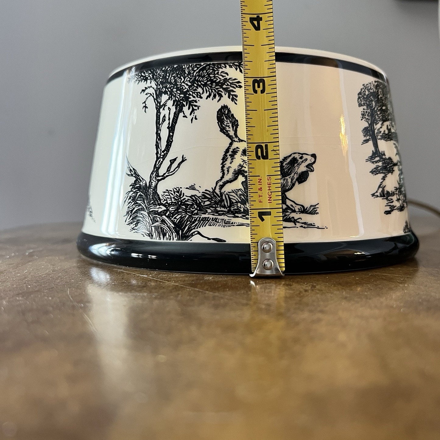 Ceramic bowl with black and white design and a measuring tape for scale on a wooden surface.