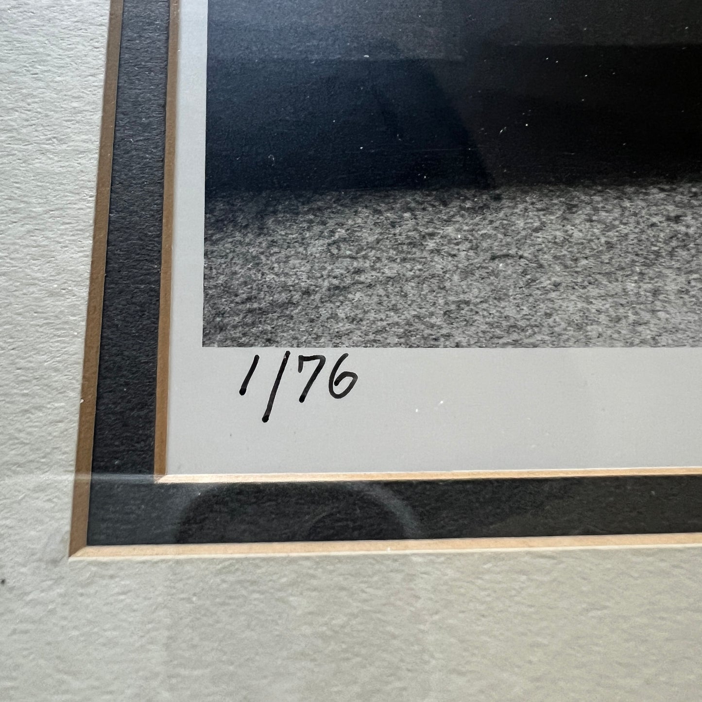 Close-up of a framed artwork showing a black-and-white textured scene with a white mat and a handwritten inscription reading '1/76' near the lower left corner.