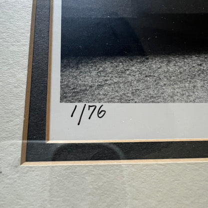 Close-up of a framed artwork showing a black-and-white textured scene with a white mat and a handwritten inscription reading '1/76' near the lower left corner.