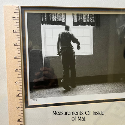 A framed black-and-white photograph showing a person standing in a room near a window, placed on a light surface with a wooden ruler along the left edge for scale. Text at the bottom reads 'Measurements Of Inside of Mat.