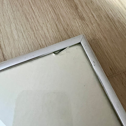 Close-up of a silver picture frame corner on a light wood floor with a chip of glass in the corner.