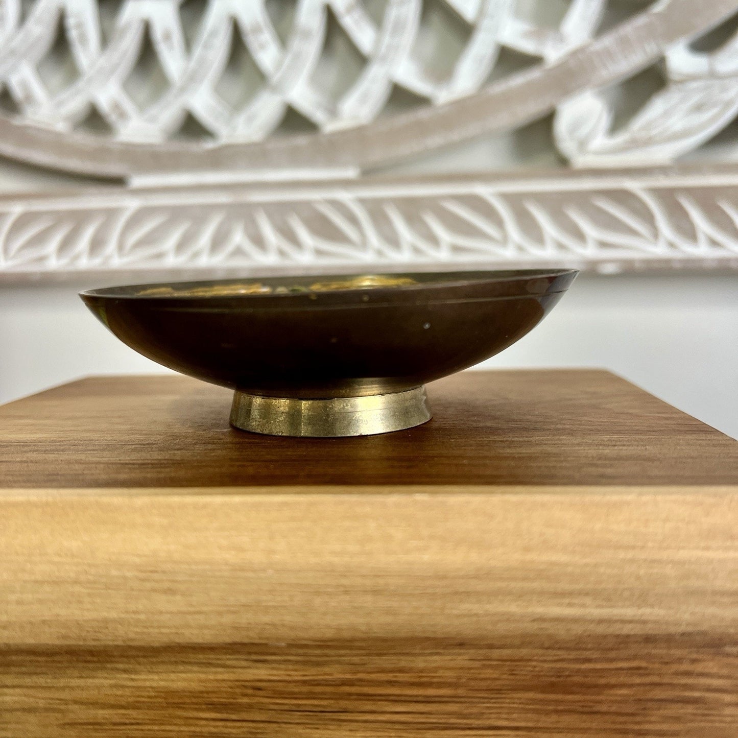 Brass bowl on a wooden surface with a white decorative item in the background