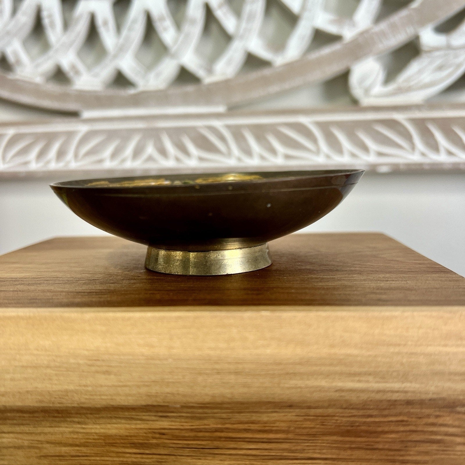 Brass bowl on a wooden surface with a white decorative item in the background