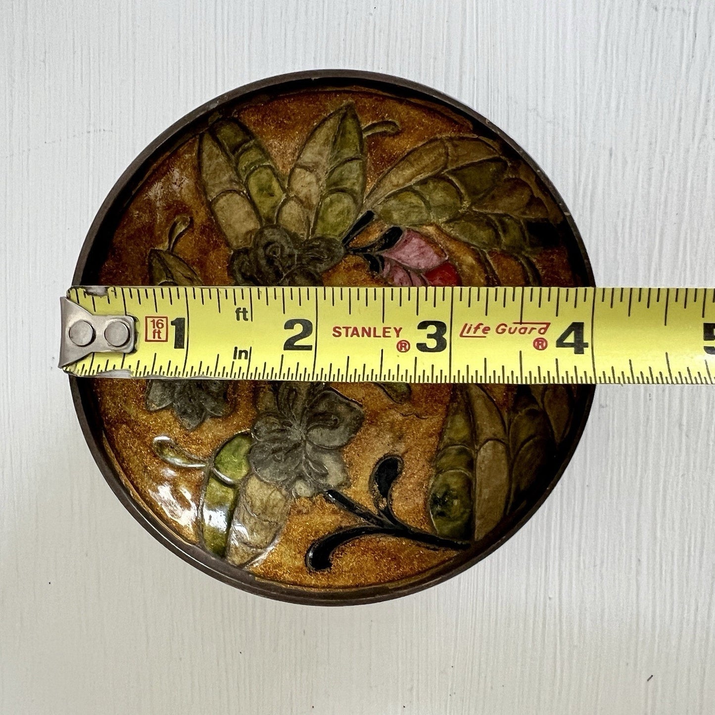 Decorative round object with floral design and a measuring tape on top